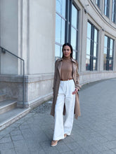 A lady wears a trench coat and white pants.